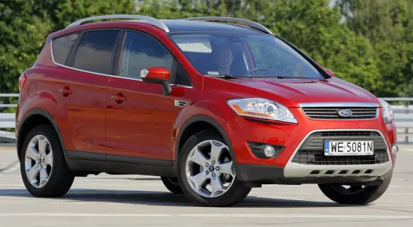 Czerwony Ford Kuga na parkingu. Kierowca w środku. Wiele osób szuka ford kuga opinie przed zakupem.