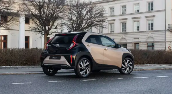 Dwukolorowy Toyota Aygo X na ulicy, z tyłu widoczny budynek z kolumnami.