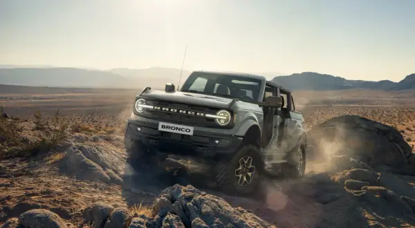 Ford Bronco pokonuje skalisty teren pustyni, wzbijając tumany kurzu.
