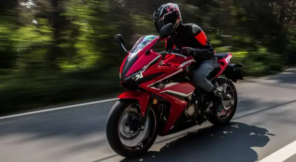 Motocyklista w kasku i kurtce jedzie sportowym, czerwonym motocyklem. Idealny sprzęt na pierwsze prawo jazdy a2.