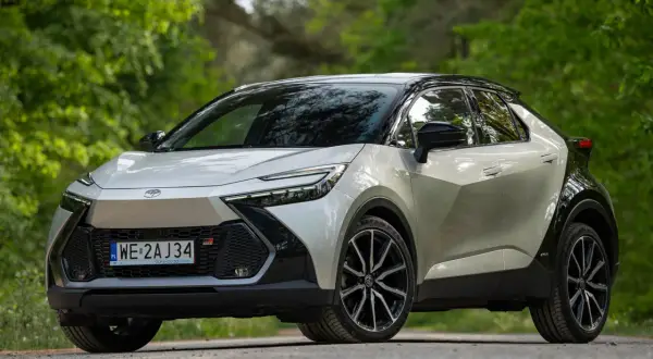 Nowy Toyota C-HR 2024 w kolorze srebrnym z czarnym dachem, zaparkowany na leśnej drodze.