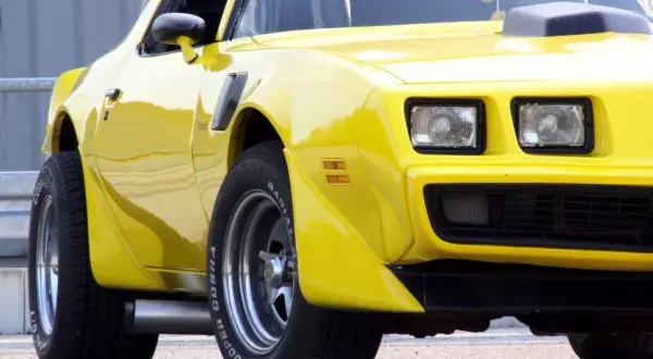 Żółty Pontiac Trans Am z lat 70. z charakterystycznym wlotem powietrza na masce i szerokimi oponami Cooper Cobra.
