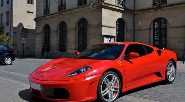 Czerwone Ferrari F430 na brukowanej ulicy przed kamienicą. Zastanawiasz się, ile kosztuje Ferrari? To marzenie wielu kierowców.