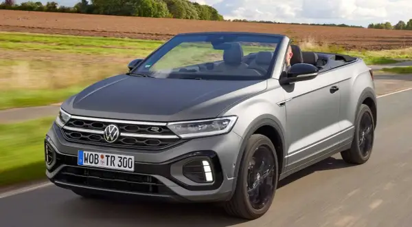 Szary Volkswagen T-Roc Cabrio jedzie po drodze, z otwartym dachem, w słoneczny dzień.