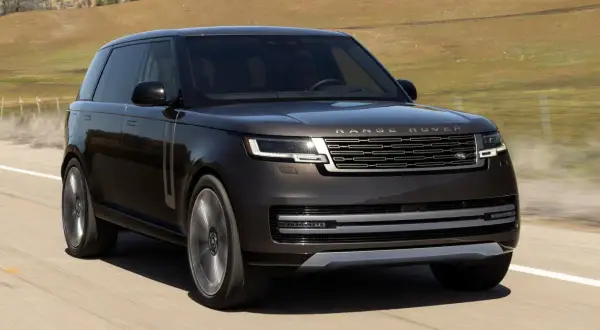 Elegancki, ciemnobrązowy Range Rover 2025 pędzi po pustej drodze, otoczony suchymi, pagórkowatymi krajobrazami.