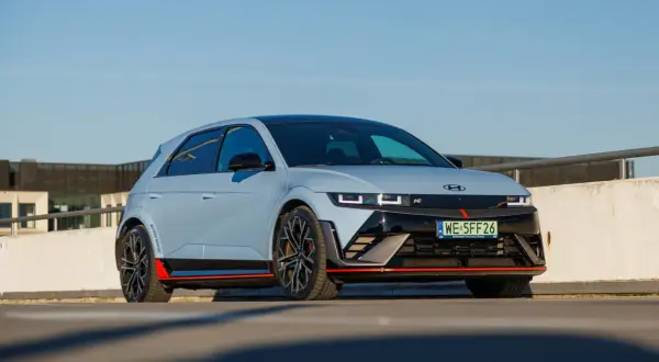 Sportowy Hyundai Ioniq 5 N z czerwonymi akcentami i czarnymi felgami na tle betonowego muru i błękitnego nieba.