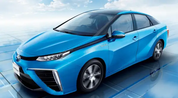 Niebieski samochód Toyota Mirai na tle błękitnego nieba z chmurami.