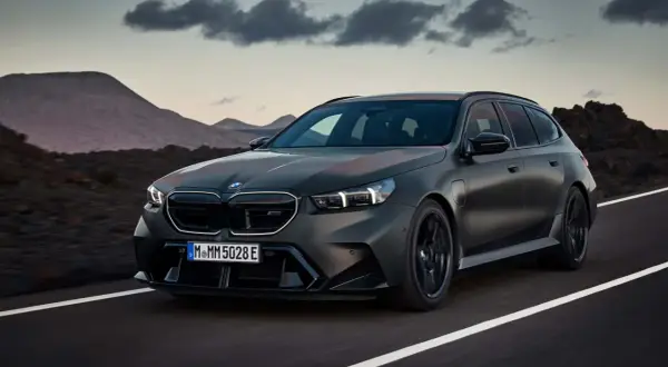 Mroczny, matowy BMW M5 Touring pędzi po pustej drodze, z górami w tle.