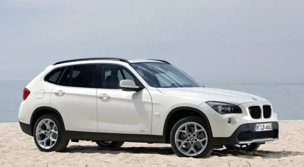 Białe BMW X1 E84 na piaszczystej plaży, z widokiem na morze w tle.