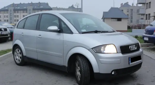 Srebrne Audi A2 zaparkowane przed blokami mieszkalnymi.