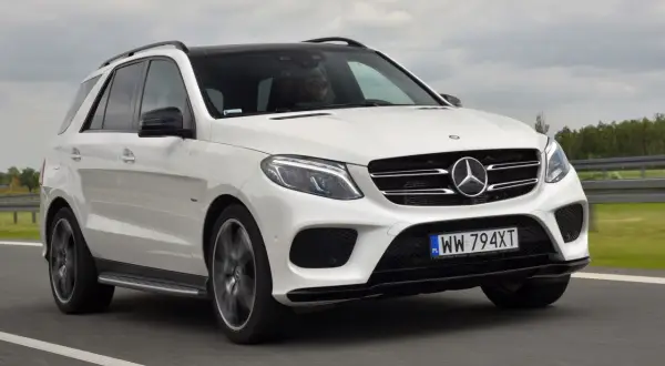 Biały Mercedes GLE 400d z czarnym dachem pędzi po drodze. Kierowca w okularach prowadzi auto.