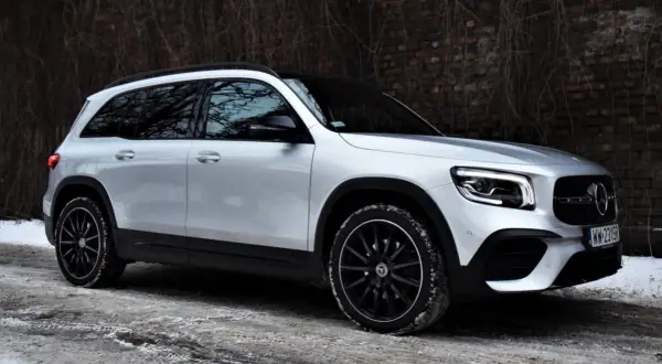 Srebrny Mercedes GLB 200 na zimowej drodze, z czarnymi felgami i przy ceglanym murze.