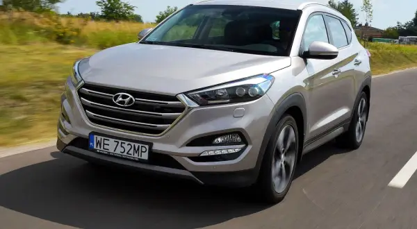 Srebrny Hyundai Tucson 2016 jedzie po drodze, otoczony zielenią.