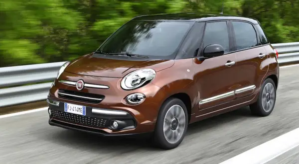 Brązowy Fiat 500L z czarnym dachem pędzi po drodze, otoczony zielenią.