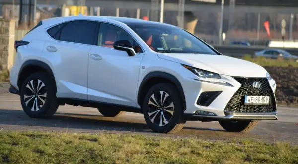 Biały Lexus NX 300 z czerwonym wnętrzem zaparkowany na tle krajobrazu.