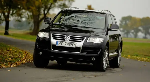 Czarny Volkswagen Touareg 2024 na jesiennej drodze, otoczony drzewami z kolorowymi liśćmi.