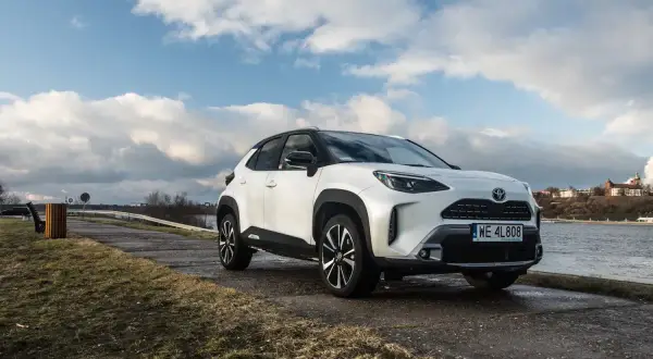 Biały Toyota Cross Yaris zaparkowany nad rzeką, z chmurami na niebie.