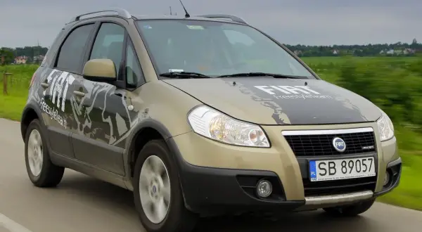 Złoty Fiat Sedici z napisem "FreestyleTeam" na masce i drzwiach jedzie po drodze.
