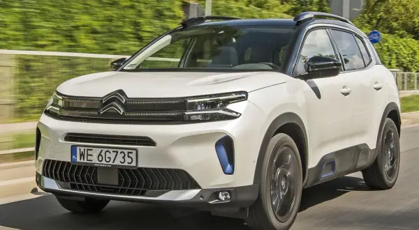 Biały Citroen C5 Aircross 2025 z czarnym dachem pędzi po drodze, otoczony zielenią.