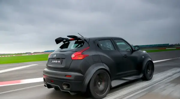Czarny Nissan Juke-R z masywnym spojlerem pędzi po torze wyścigowym, zostawiając za sobą smugę rozmytych linii.