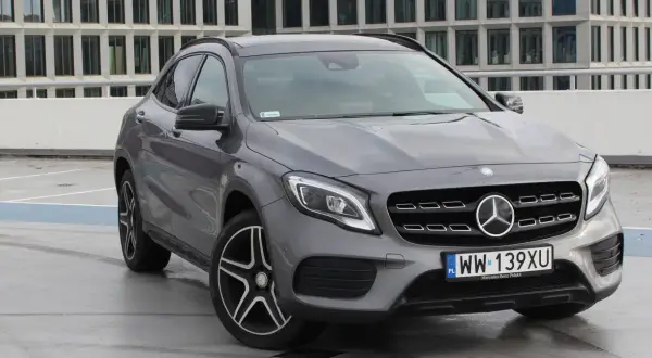 Szary Mercedes GLA 220 z polskimi tablicami rejestracyjnymi stoi na parkingu przed nowoczesnym budynkiem.