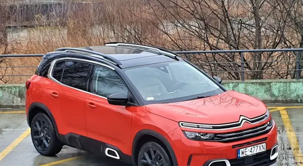 Pomarańczowy Citroen C5 Aircross z czarnym dachem stoi na mokrym parkingu.