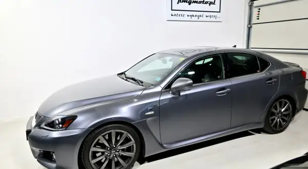 Szary Lexus IS F w garażu, z logo "pmgmotopl" na ścianie.