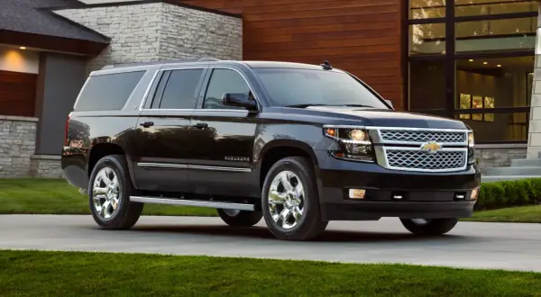 Czarny Chevrolet Suburban na podjeździe przed nowoczesnym, podmiejskim domem z kamiennymi i drewnianymi elementami.