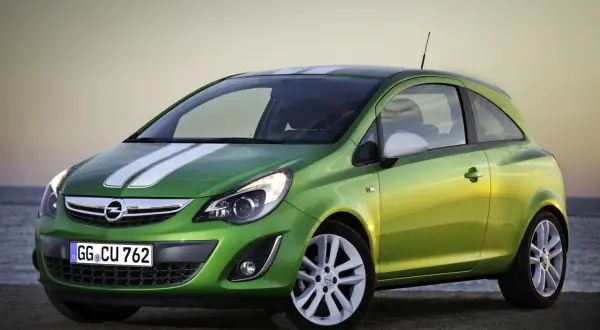 Zielony Opel Corsa D 1.2 benzyna z białymi pasami na masce, zaparkowany przy plaży.