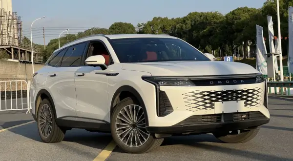 Biały OMODA 9 Super Hybrid z czerwonym wnętrzem stoi na drodze, z drzewami i budynkami w tle.