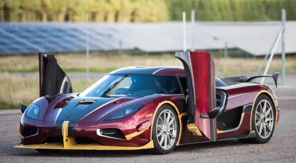 Czerwony Koenigsegg Agera RS z otwartymi drzwiami, gotowy do startu na tle paneli słonecznych.