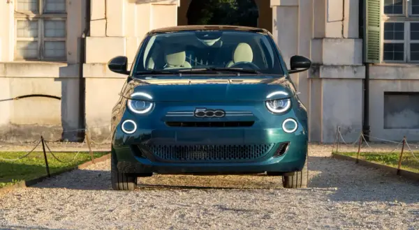 Nowy Fiat 500 w kolorze głębokiej zieleni, z charakterystycznymi okrągłymi światłami, zaparkowany przed zabytkowym budynkiem. Sprawdź aktualną fiat 500 cena!