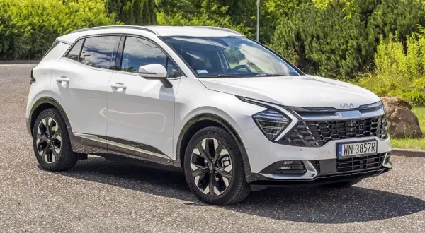 Biały Kia Sportage 1.6 benzyna zaparkowany na tle zieleni. Nowoczesny design i eleganckie felgi.
