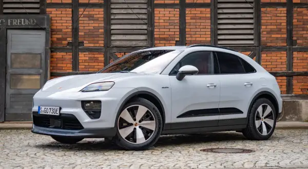 Biały Porsche Macan Electric na bruku przed ceglanym budynkiem. Sprawdź aktualną porsche macan cena.