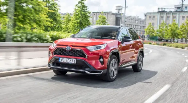 Czerwony Toyota RAV4 2024 na zakręcie drogi, z kierowcą za kierownicą.