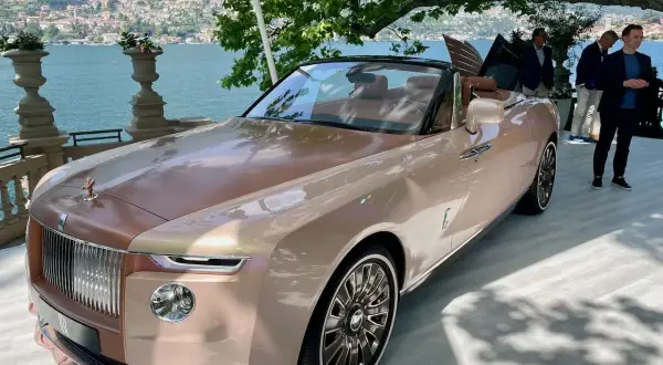 Elegancki Rolls-Royce Boat Tail w kolorze szampańskim, prezentowany nad jeziorem Como, przyciąga wzrok swoim unikalnym designem.