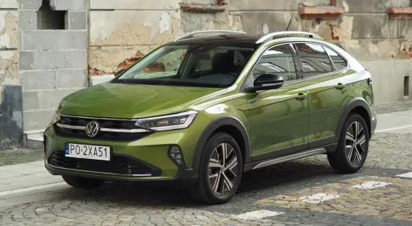 Zielony Volkswagen Taigo na brukowanej ulicy, z charakterystycznym dachem i felgami.