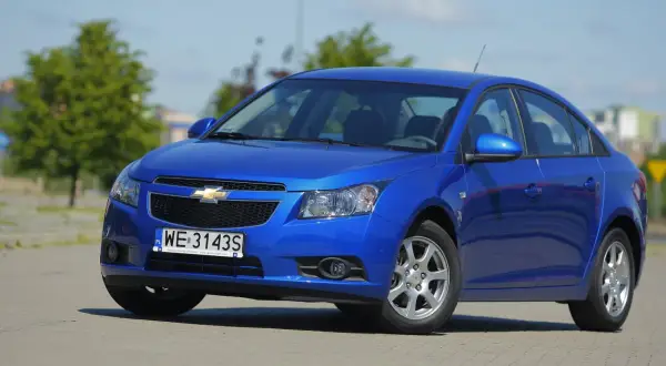 Błękitny Chevrolet Cruze 1.8 benzyna zaparkowany na placu.