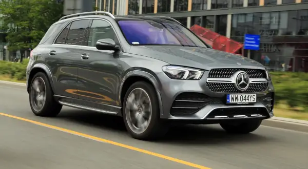 Szary Mercedes GLE 300d jedzie po drodze, w tle nowoczesne budynki.