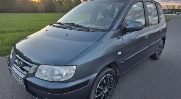 Szary Hyundai Matrix na tle zachodzącego słońca i zielonej łąki.