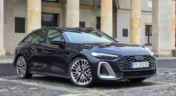 Elegancki, ciemnogranatowy Audi A5 Avant 2025 z charakterystycznym grillem i felgami stoi przed zabytkową budowlą.