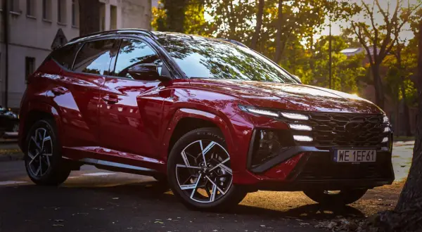 Czerwony Hyundai Tucson 2023 z czarnymi felgami i przyciemnianymi szybami, zaparkowany na tle kamienicy i drzew w jesiennym słońcu.
