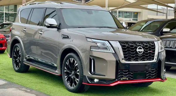 Szary Nissan Patrol 2025 Nismo z czerwonymi akcentami, prezentujący się na zielonej trawie.