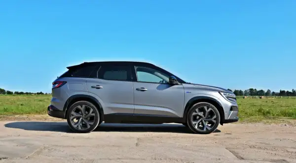 Srebrny Renault Austral z czarnym dachem stoi na polnej drodze, w tle zielone pole i błękitne niebo.