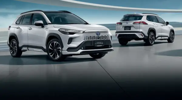 Dwa białe SUV-y Toyota Corolla Cross 2025 stoją na betonowej podłodze, jeden z przodu, drugi z tyłu.