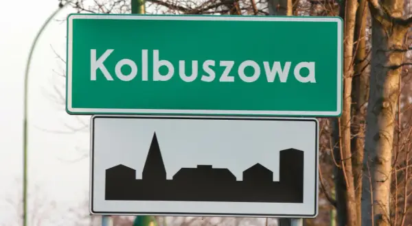 Znak drogowy z napisem Kolbuszowa i sylwetką miasta. To znak d42, informujący o wjeździe do miejscowości.