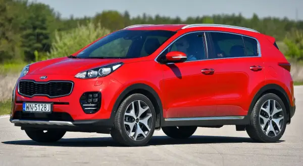 Czerwony Kia Sportage 1. generacji z kierowcą w okularach przeciwsłonecznych jedzie po drodze.