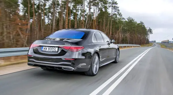 Czarny Mercedes S400d 4Matic z tablicą WW 800SL jedzie po drodze wśród drzew.