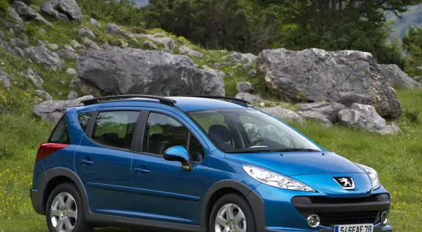 Niebieski Peugeot 207 SW na tle skalistego, zielonego krajobrazu. Idealny na wycieczkę poza miasto.