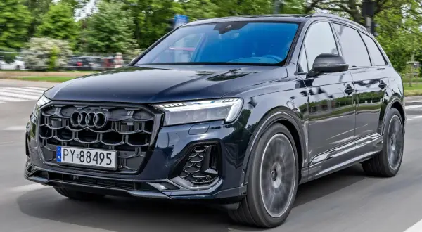 Ciemny Audi Q7 w ruchu ulicznym, z grillem i światłami LED. Sprawdź audi q7 cena i możliwości tego luksusowego SUV-a.